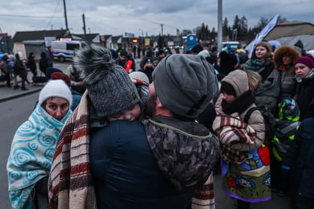 A man who fled the war in Ukraine holds a baby as they wait in line to board a bus with Police officers (Photo: Getty)