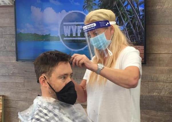 Gilly Carter gives a customer a haircut with visor and mask on at her barber shop, The Men's Room