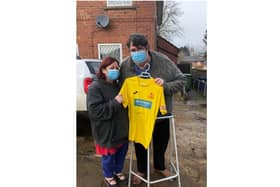 Julie Hyde stands next to Ben Cox, as he holds the autographed Banbury United Football Club jersey which has boosted his spirits while he battles long Covid