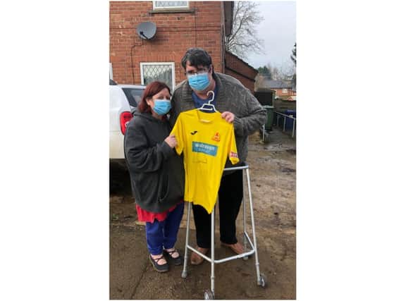 Julie Hyde stands next to Ben Cox, as he holds the autographed Banbury United Football Club jersey which has boosted his spirits while he battles long Covid
