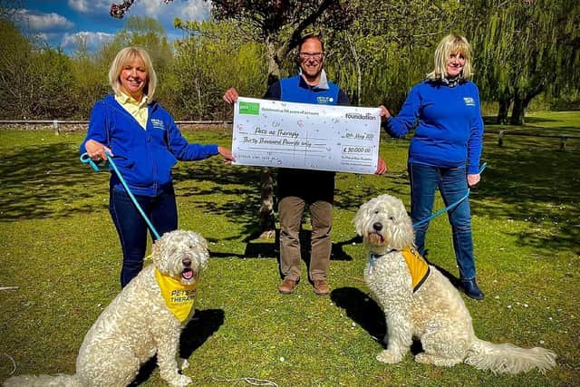 Pets As Therapy receives cheque from The Pets at Home Foundation. From L-R: Sarah Mackie with Lola (Labradoodle), Matthew Robinson with 30,000 cheque, Julie Edwards with Rupert (Goldendoodle))