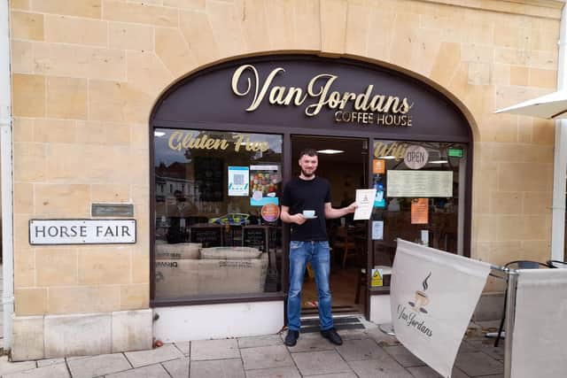 Head barista Aidan Booth holds a coffee and the latest menu for VanJordans 
Coffee House and café.