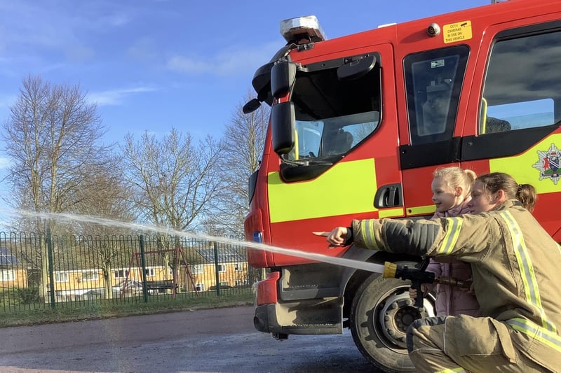 Orchard Fields pupil Layla being taught how to use the hose pipe by one of the special guests.