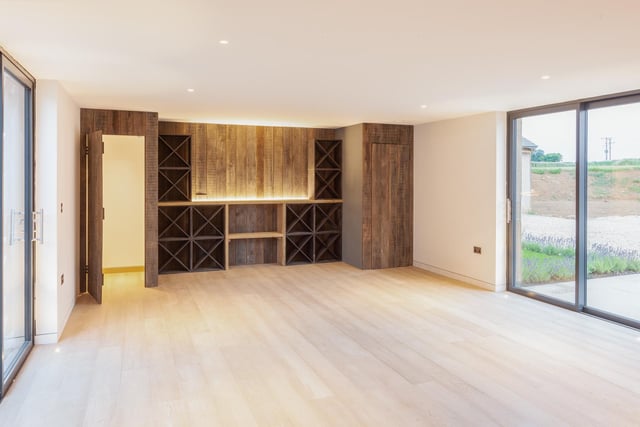 The drawing room has oak flooring and dual sliding glazed doors to the front and rear with an illuminated glass fronted wine room to one end.