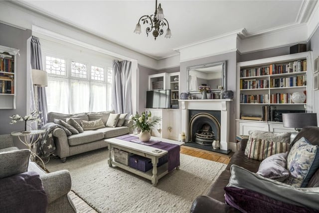 An elegant sitting room features a bay window with stained glass, traditional wooden floorboards, in-built storage and a fireplace with gas fire.