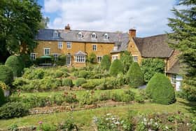 The house's tiered garden leads down to a garden and large lawn with several mature trees and a stream.