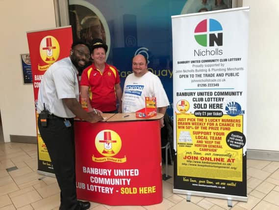 Ola Smith buys a lottery ticket from Banbury Utd supporter-volunteers Richard 'Lofty' Phillips and Kevin Preedy
